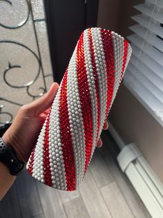 a hand is holding a red, white and blue beaded vase in front of a window