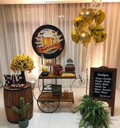 a table topped with balloons next to a sign and potted plants in front of a window