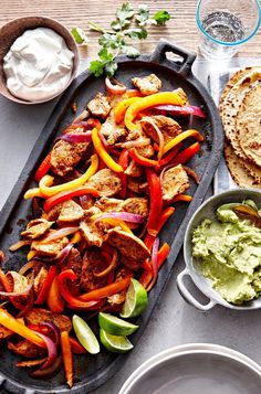 a platter filled with meat, vegetables and guacamole next to pita bread