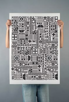 a person holding up a black and white art print with geometric designs on the front