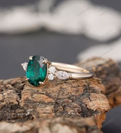 an emerald and diamond ring sitting on top of a rock