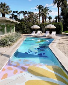 an empty swimming pool surrounded by palm trees and lawn chairs with umbrellas in the background