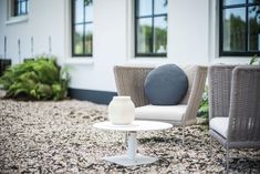 two chairs and a table sitting in front of a white building with windows on the side