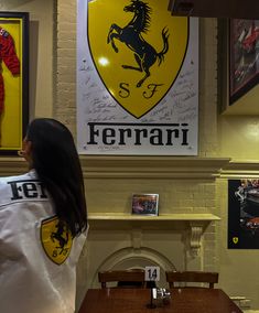 a woman standing in front of a ferrari logo on a wall next to a table