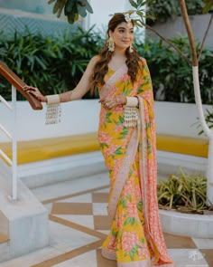 a woman in a yellow and pink sari standing next to some stairs with her hand on the railing