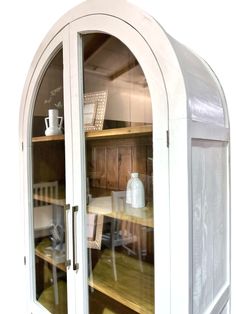 an arched glass cabinet with wooden shelves and chairs