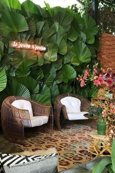 two wicker chairs sitting next to each other in front of a green plant wall