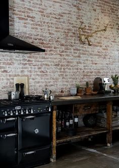 a kitchen with an oven, stove and table in front of a brick wall that has potted plants on it