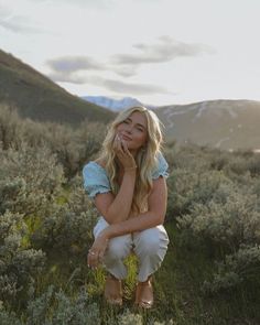 a woman sitting in the grass with her hand on her face and looking at the camera