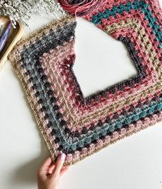 a hand is holding a crocheted square in front of some yarn and scissors