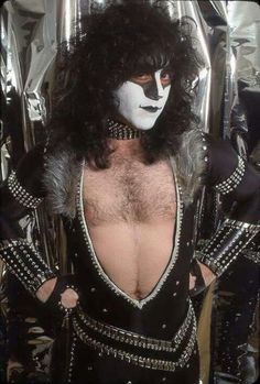 a man with black hair and white face paint on his chest, wearing a costume