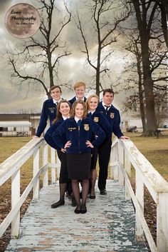 a group of young people standing on top of a wooden bridge in front of trees