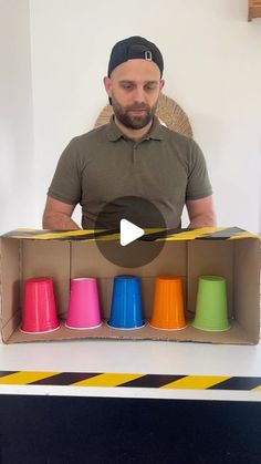 a man sitting at a table in front of a box filled with colorful plastic cups