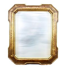 an ornate gold framed mirror on a white wall with clouds in the sky behind it