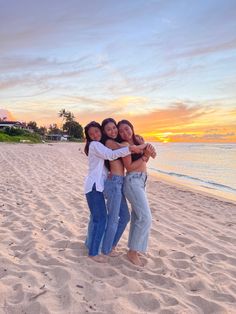 three women hugging on the beach at sunset