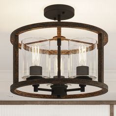 This 3-light semi-flush mount illuminates any room with a warm, ambient glow. The central candelabra fixture as well as the open cylindrical frame are crafted from steel with a two-tone finish of black and a wood-look hue for a mix of modern and farmhouse. Three 60W max bulbs (sold separately) are surrounded by clear glass cylindrical shades that reflect light throughout your space. With a hanging height of 14", this mount is ideal for smaller areas with low ceilings. The dimmer switch can also Rustic Dining Room Lighting Over Table, Ski Cottage, Semi-flush Mount Lights, Farmhouse Light Fixtures, Entryway Lighting, Low Ceilings, Flush Mount Lights, Glass Ceiling Lights, Light Fixtures Flush Mount