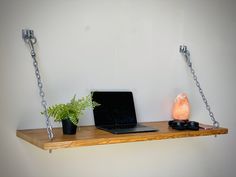 a laptop computer sitting on top of a wooden shelf next to a plant and phone