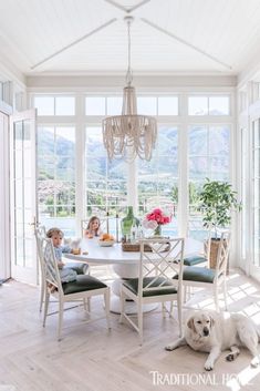 two children and a dog sitting at a table in a room with large glass windows