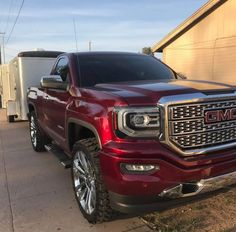 a red gmc truck parked in front of a building next to a white trailer