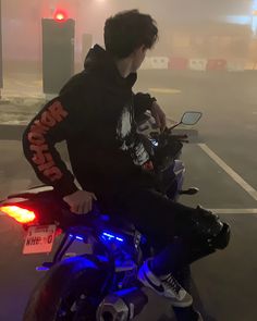 a young man riding on the back of a motorcycle in a parking lot at night