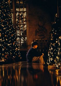 a person sitting on the floor in front of a christmas tree looking at their cell phone