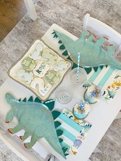 a table topped with plates and cups filled with dinosaur themed desserts on top of it