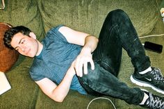 a young man laying on top of a green couch next to a laptop and headphones