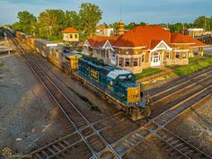 a train is traveling down the tracks in front of some houses and trees with red roof tops