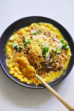 a black bowl filled with food on top of a white table next to a wooden spoon