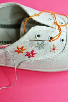 a pair of white shoes with colorful flowers on the laces are sitting on a pink surface