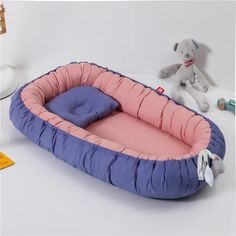 a pink and blue dog bed next to a teddy bear on a white table with stuffed animals