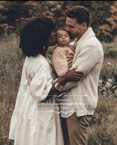 a man and woman are holding a baby in their arms while standing in the grass