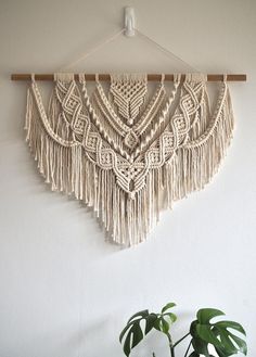 a macrame wall hanging on a white wall next to a potted plant