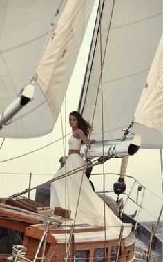 a woman in a white dress standing on the deck of a sailboat with sails down