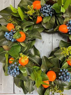 a wreath with oranges, blue berries and green leaves on a white wooden background