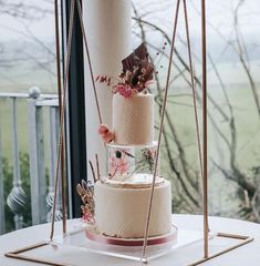 three tiered wedding cake with flowers on the top and bottom, sitting on a table in front of a window