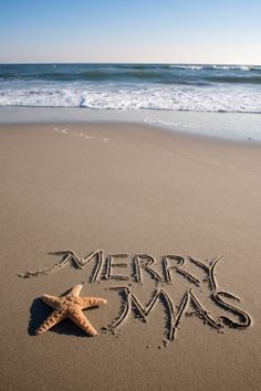 merry christmas written in the sand at the beach with a starfish on it's side