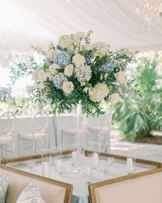 a vase with white and blue flowers sitting on top of a table next to chairs