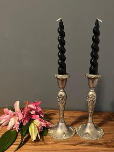 two silver candlesticks sitting on top of a wooden table next to a pink flower