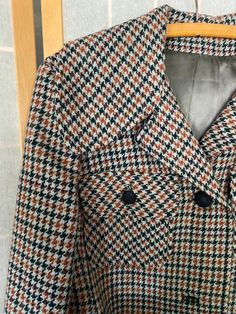 "1970's Juli de aroma houndstooth coat with a blue belt. Belt is made of a faux leather material that, being 50 years old, is now a little sticky to the touch and flakes off in the hand. Missing buttons 2 and 4 and the left pocket buttons. Bust: 40\" Shoulder to hem: 41\"" Brown Houndstooth Winter Outerwear, Brown Houndstooth Outerwear For Winter, Brown Houndstooth Outerwear For Fall, Retro Belted Fall Outerwear, Retro Belted Outerwear For Fall, Retro Business Outerwear For Fall, Retro Lined Outerwear For Fall, Notch Lapel Houndstooth Outerwear For Fall, Notch Lapel Outerwear With Houndstooth Pattern For Fall