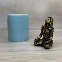 a gold and black buddha statue next to a blue mug on a wooden table with a white wall in the background