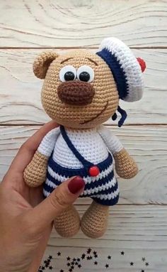 a crocheted teddy bear wearing a hat and overalls is being held up by someone's hand