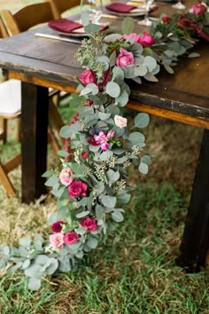 the table is set with pink flowers and greenery on it, along with silverware