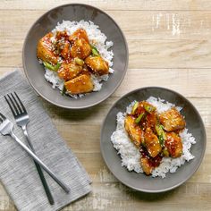 two plates filled with rice and chicken on top of a wooden table next to silverware