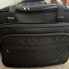 a black piece of luggage sitting on top of a carpeted floor next to a wall