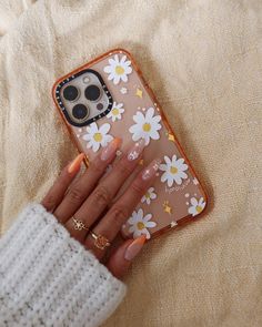 a woman's hand holding an iphone case with daisies on it and orange nail polish