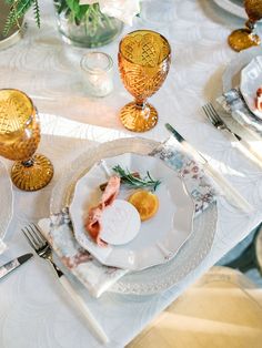 the table is set with plates, silverware and gold vases on top of it