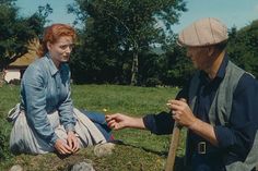 a man and woman sitting on the ground next to each other in a grassy field