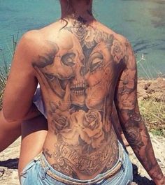 a woman with tattoos on her back sitting next to the ocean