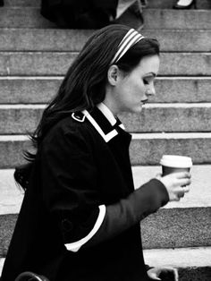 a woman walking down the street with a coffee cup in her hand and another person sitting next to her